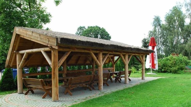 A wooden pavilion with benches and a thatched roof, surrounded by a paved area and greenery. - Hotel U Witaszka (Czosnów)