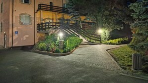 A building with a staircase leading to a balcony, surrounded by greenery and a paved path. - Hotel U Witaszka (Czosnów)
