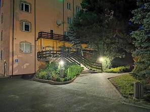 A building with a staircase leading to a balcony, surrounded by greenery and a paved path. - Hotel U Witaszka (Czosnów)