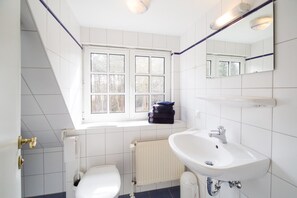 A bathroom with a white toilet, a sink, a window, and a radiator. - Ferienwohnungen Familie Outzen (Nebel)