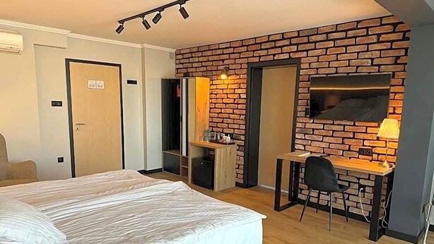 A hotel room with a bed, a desk, a chair, a TV, and a brick wall.
