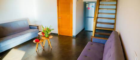 A modern living room with a sofa, a small table with a plant, and a wooden staircase.