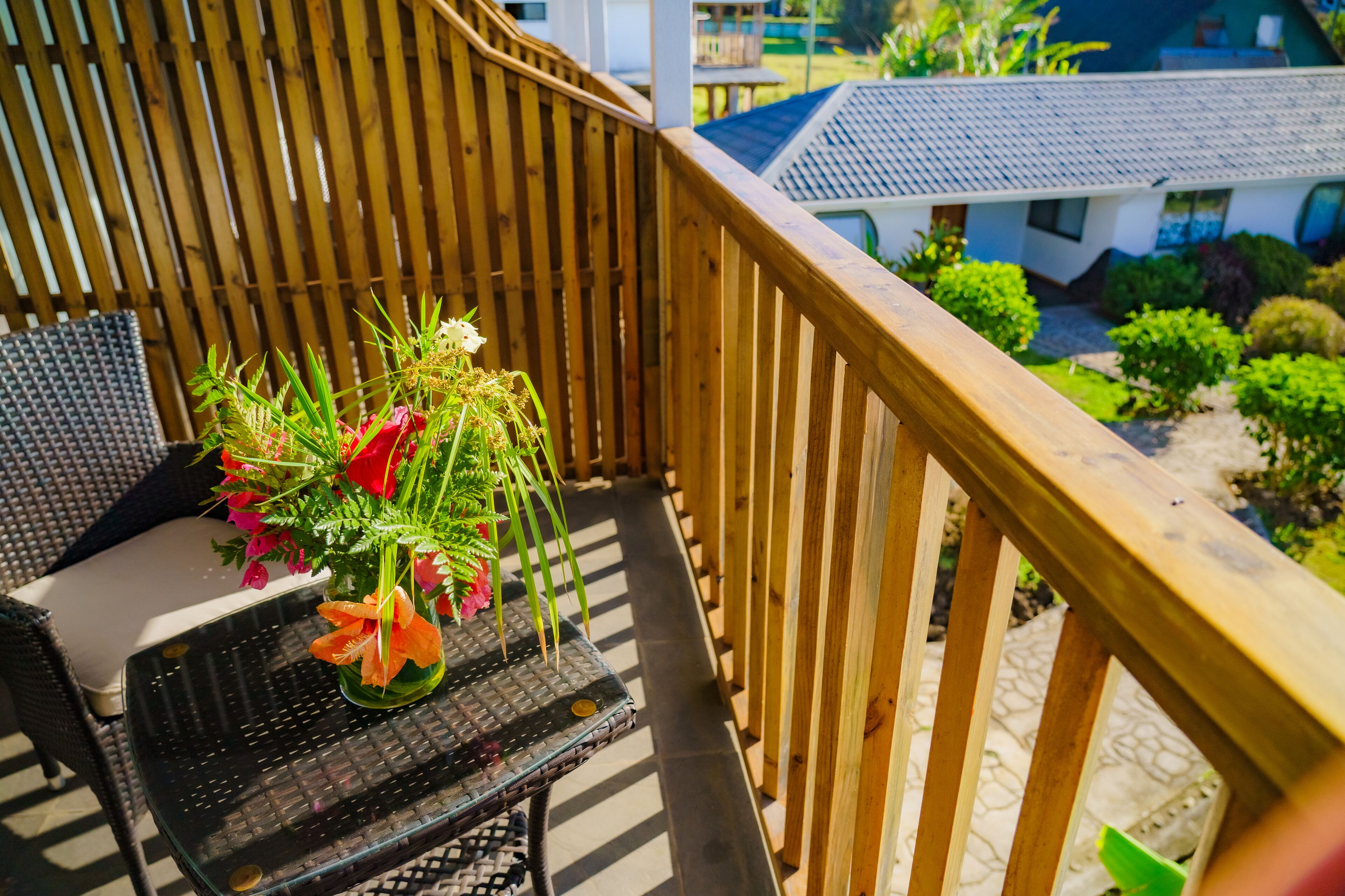 A balcony with a wooden railing, a wicker chair, and a small table with a vase of flowers.