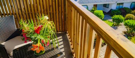 A balcony with a wooden railing, a wicker chair, and a small table with a vase of flowers.