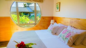 Een hotelkamer met een groot bed, een rond raam en uitzicht op groen.