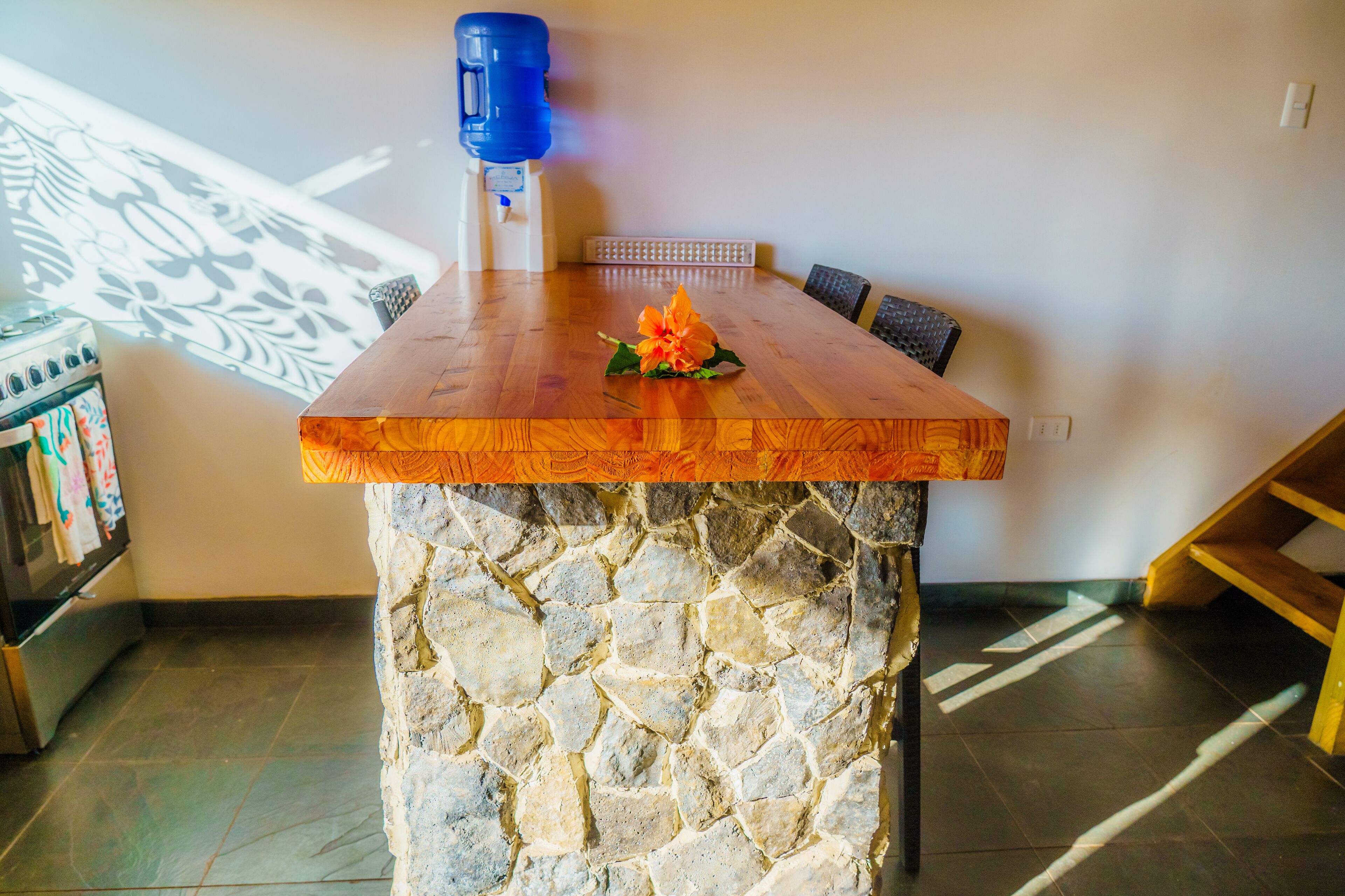 Ein Holztisch mit Steinsockel, ein blauer Wasserspender und eine Wand mit Muster im Hintergrund.