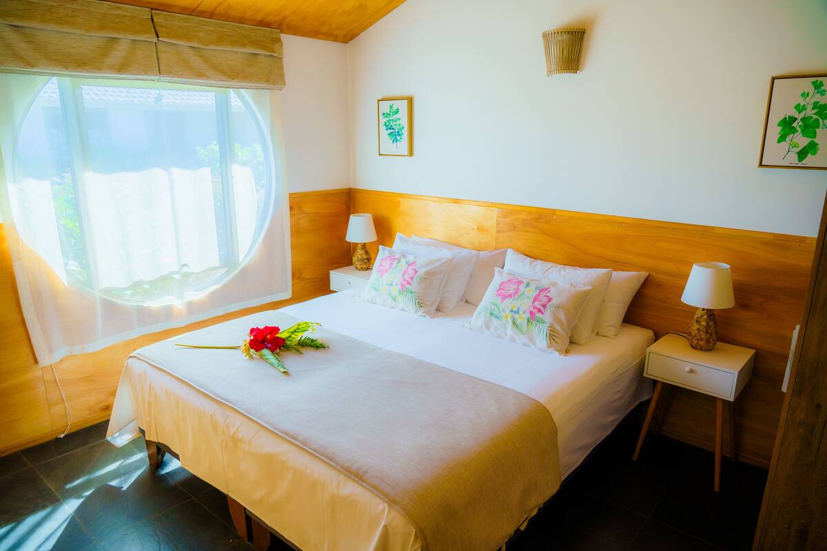 A neatly made bed with floral pillows, a bedside lamp, and a window with curtains.
