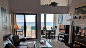 A living room with a sofa, coffee table, and a TV. There is a balcony with a view of the beach. - Palm Beach Club by Surfside VR (Pensacola Beach)