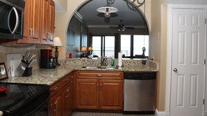 A kitchen with wooden cabinets, a granite countertop, a dishwasher, and a microwave. - Palm Beach Club by Surfside VR (Pensacola Beach)