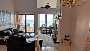 A spacious living room with a leather sofa, a glass coffee table, and a view of the sea through large windows. - Palm Beach Club by Surfside VR (Pensacola Beach)