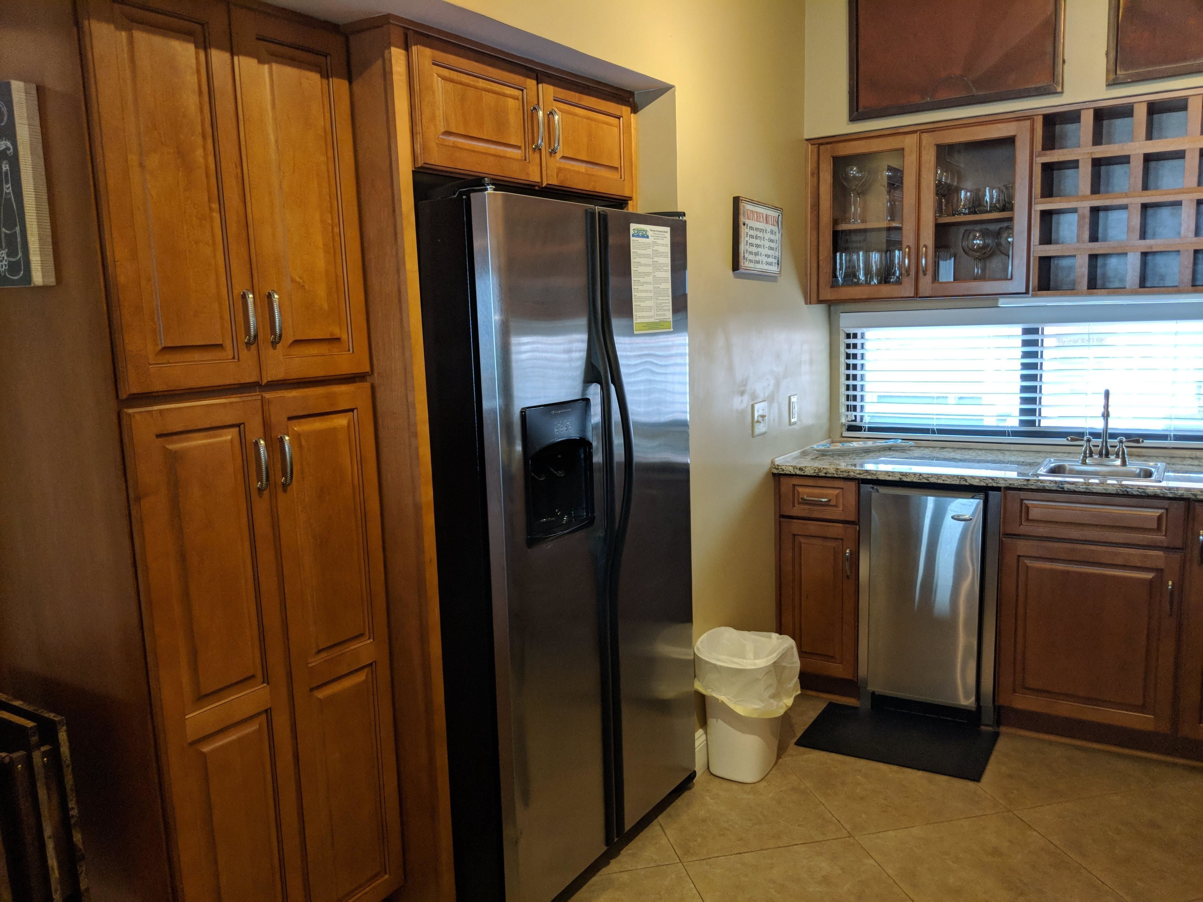 A kitchen with wooden cabinets, a stainless steel refrigerator, a dishwasher, and a window with blinds.