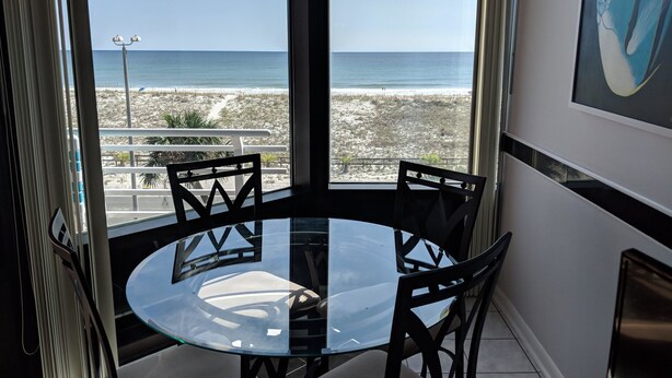 A glass table with chairs in a room with a view of the beach and ocean. - Palm Beach Club by Surfside VR (Pensacola Beach)