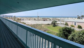 A view from a balcony overlooking a parking lot, a building, and a beach with palm trees. - Deep Water Cove by Surfside VR (Pensacola Beach)