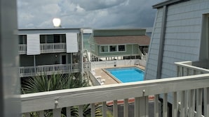 A view of a swimming pool area with a building in the background. - Boardwalk by Surfside VR (Pensacola Beach)
