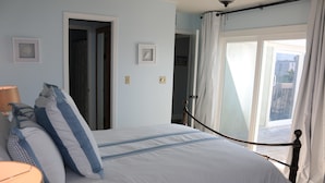A bedroom with a bed, a lamp, and a view of the outside. - Boardwalk by Surfside VR (Pensacola Beach)
