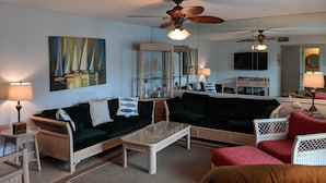 A living room with wicker furniture, a painting of sailboats, and ceiling fans. - Boardwalk by Surfside VR (Pensacola Beach)