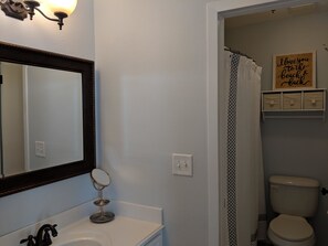 A bathroom with a white sink, a mirror, a light fixture, a toilet, and a shower curtain.