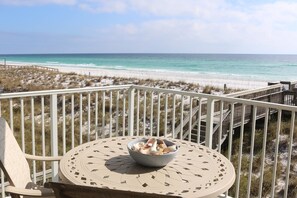 A balcony with a table and a bowl of snacks, overlooking a beach with a wooden walkway. - Starboard Village by Surfside VR (Pensacola Beach)