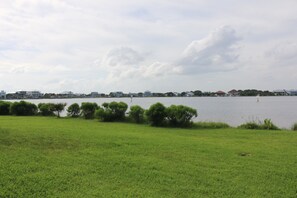 A grassy field with a body of water and buildings in the background.