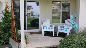 A covered porch with two white chairs and a small table, a wooden ladder, and a decorative metal sculpture. - Sand Dollar by Surfside VR (Pensacola Beach)