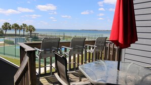 Uma varanda com mesa e cadeiras de vidro, com vista para uma piscina e para o mar.