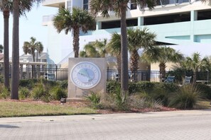 Une enseigne avec le mot « Dolphin » et une illustration de dauphin, entourée de palmiers et d’un bâtiment en arrière-plan.