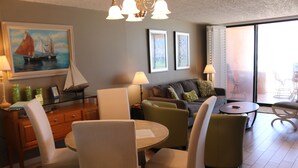 Un salon moderne comprenant un coin repas, un ensemble de canapés et un tableau représentant un voilier.