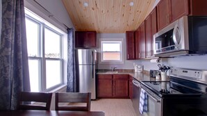 Una cocina con armarios de madera, electrodomésticos de acero inoxidable y un ventanal con cortinas.