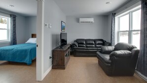 Una habitación con una cama, un sofá de cuero negro, un armario de madera y un televisor.