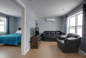 Una habitación con una cama, un sofá de cuero negro, un armario de madera y un televisor.