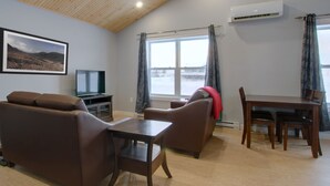 Una sala de estar con un sofá, una mesa, un televisor y una ventana con cortinas.