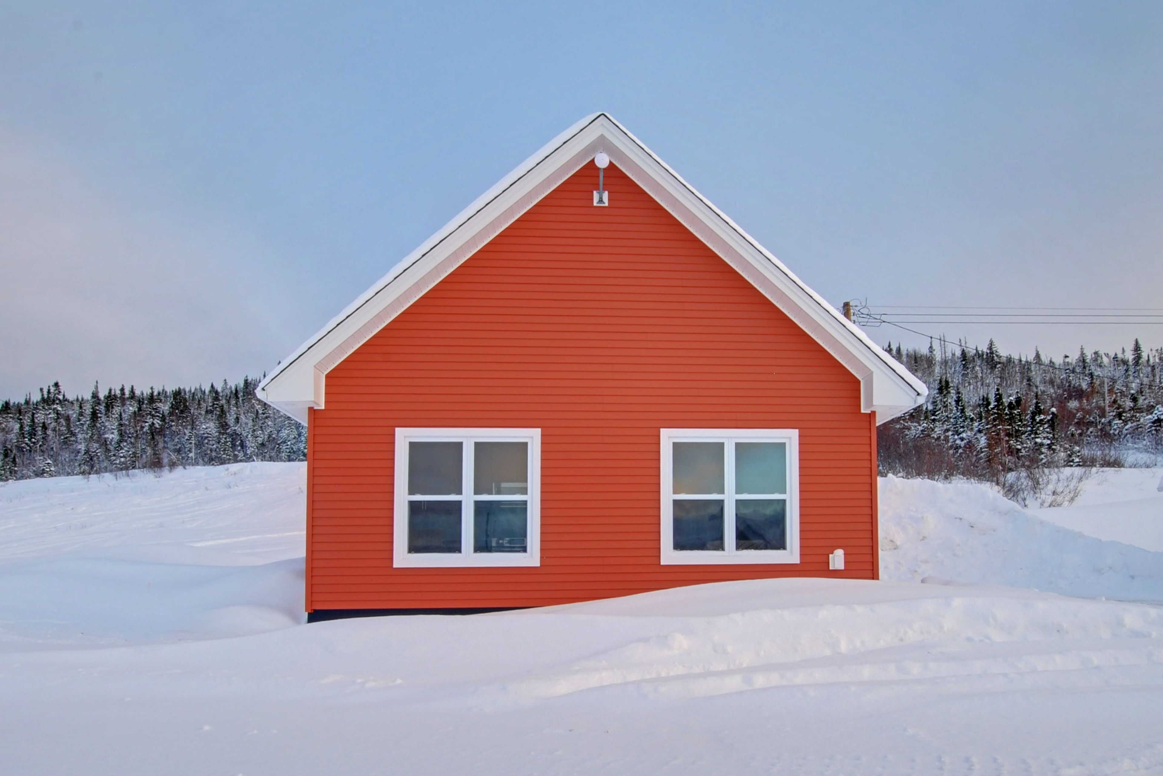 Una casa roja con techo a dos aguas y dos ventanas, rodeada de árboles cubiertos de nieve.