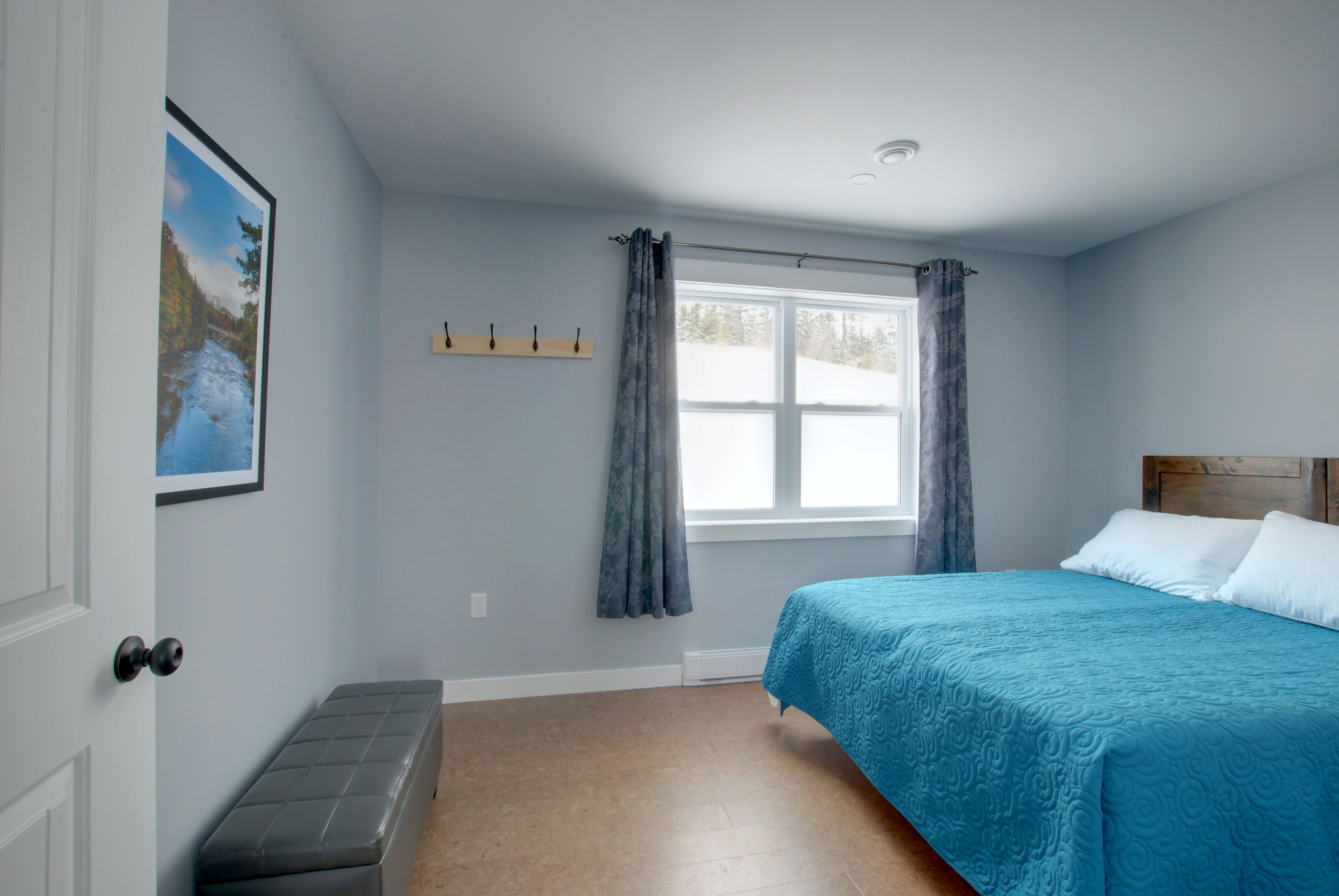 A bedroom with a bed, a bench, a window with curtains, a coat rack, and a painting on the wall.