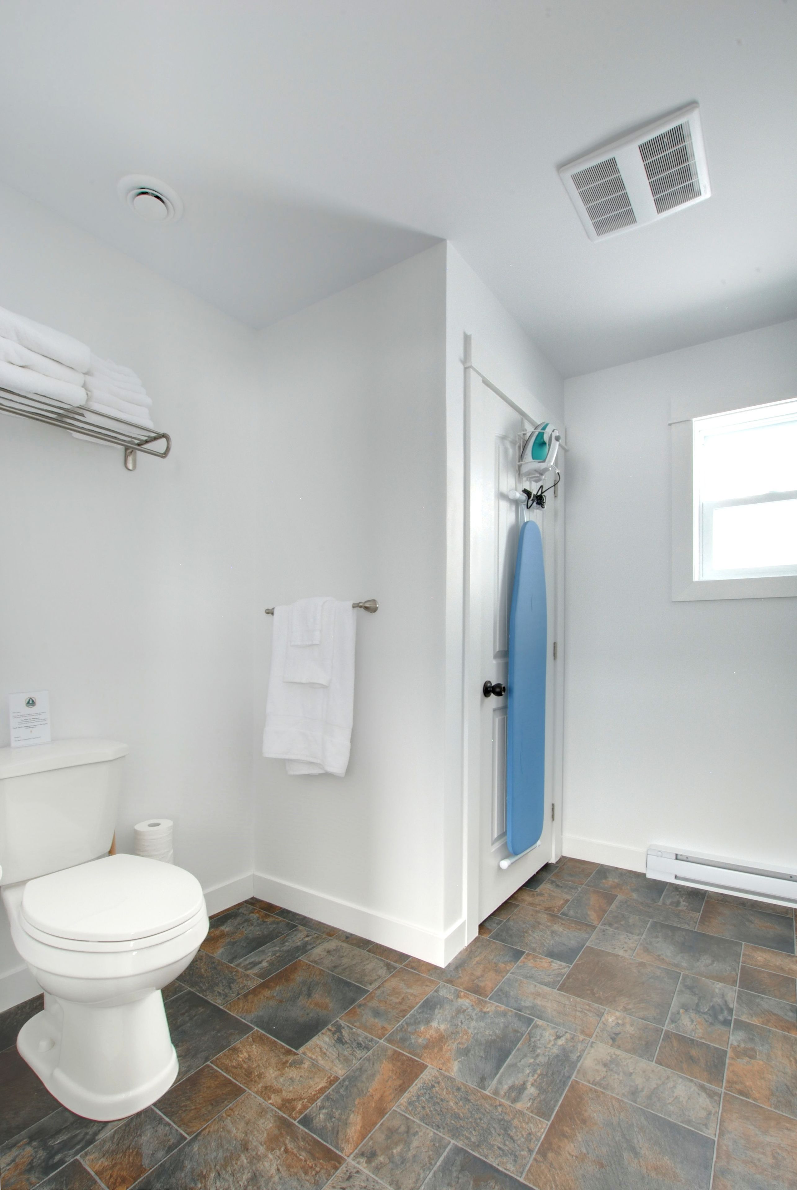 A bathroom with a white toilet, a blue shower door, and a tiled floor.