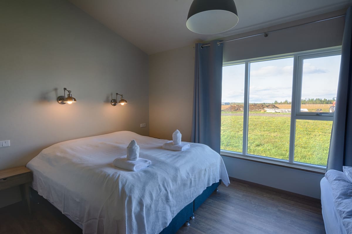 A bedroom with a large bed, two wall-mounted lights, a window with a view of the outdoors, and a bedside table.