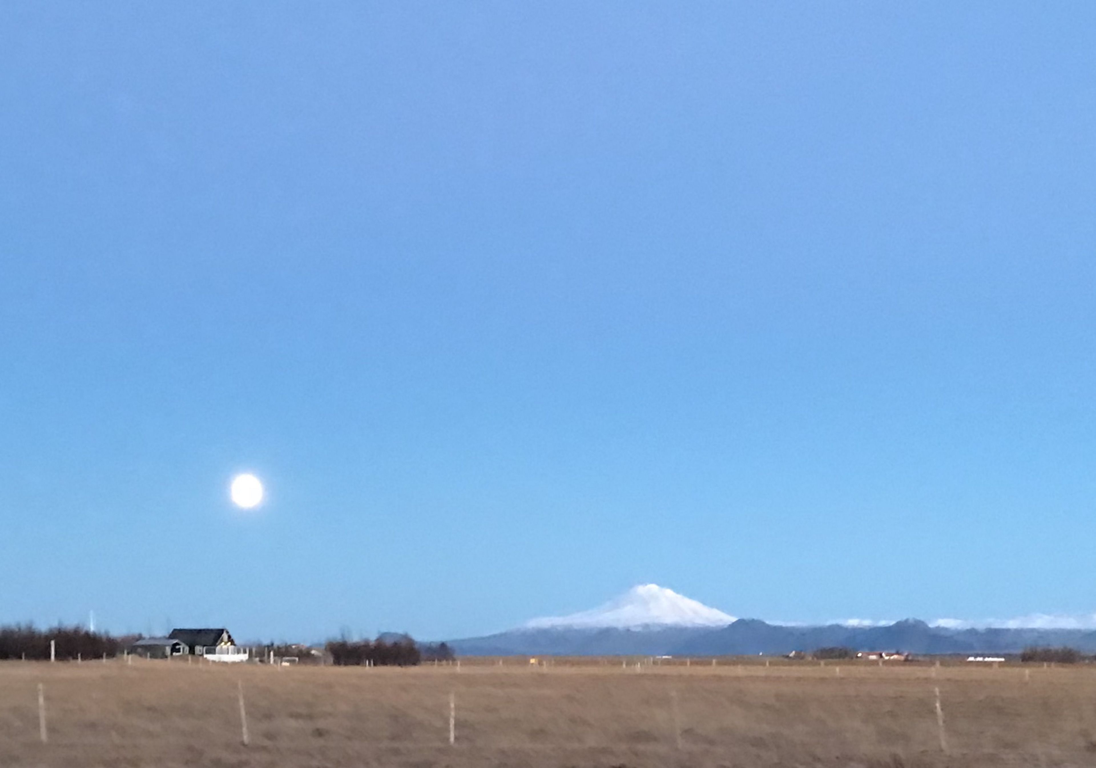 A rural landscape with a house, a field, and a mountain in the distance.