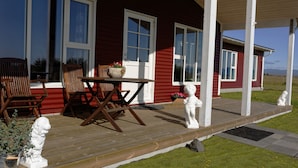 Una casa roja con terraza de madera, columnas blancas y una estatua de un perro.