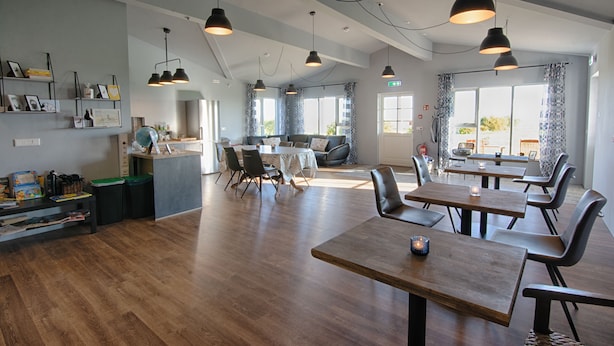 Un comedor amplio con mesas y sillas de madera, iluminación colgante y vistas al exterior a través de amplios ventanales.