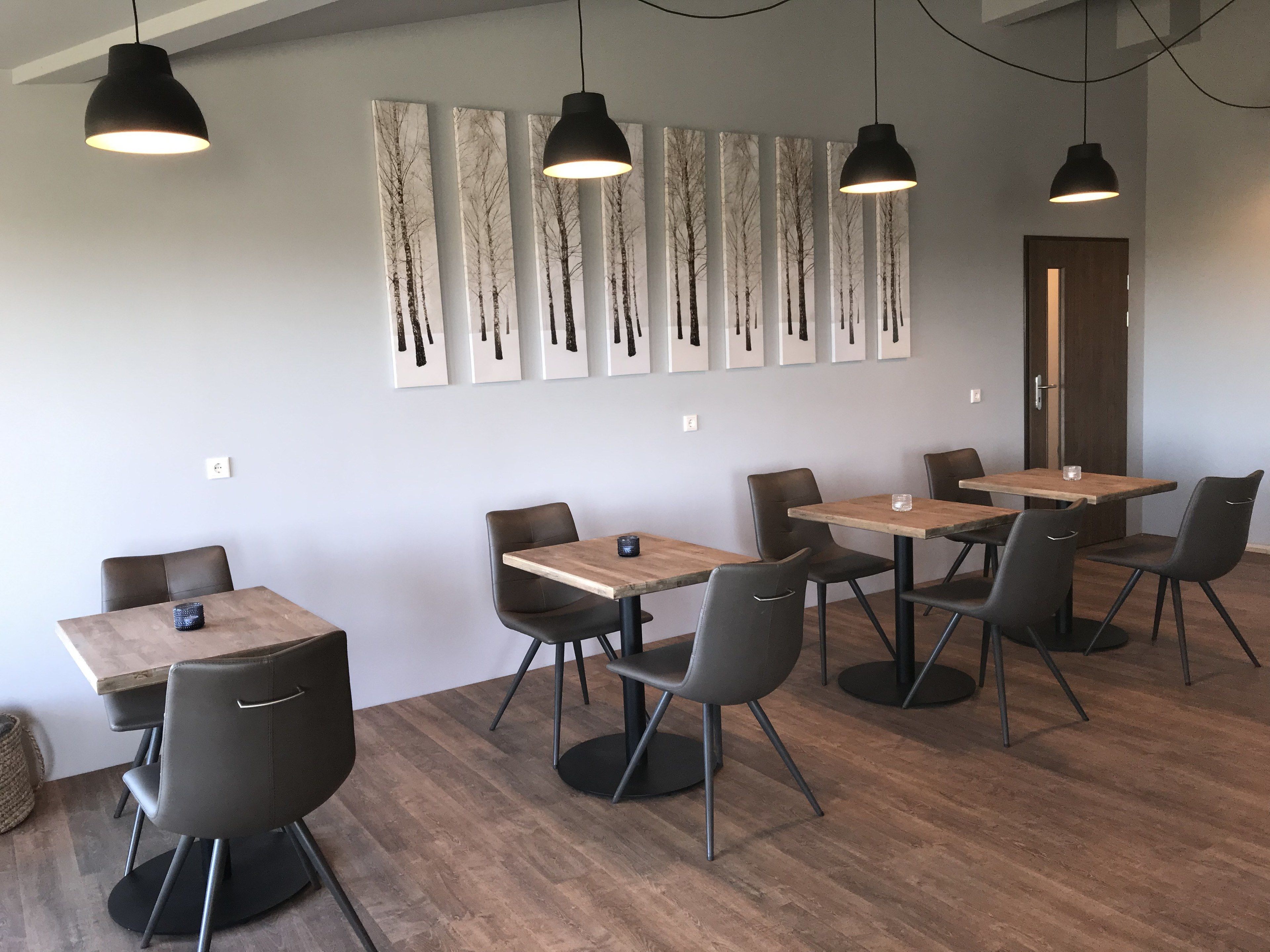 A modern dining area with wooden tables and black chairs, featuring a series of vertical paintings on the wall.