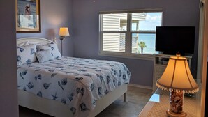 Ein Schlafzimmer mit einem Bett, einem Deckenventilator, einem Fenster mit Jalousien, einem Fernseher und einer Lampe.