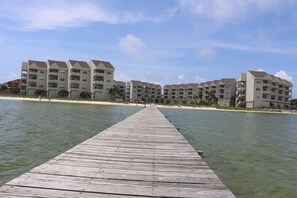 A wooden pier leading to a beachfront hotel with multiple balconies and a clear sky. - Baywatch by Surfside VR (Pensacola Beach)