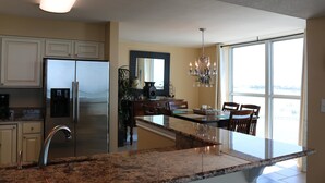 A modern kitchen with granite countertops, stainless steel appliances, and a large window providing a view. - Tristan Towers by Surfside VR (Pensacola Beach)