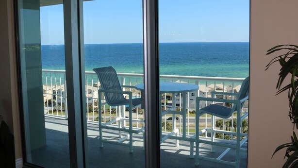 A balcony with white chairs and a table, overlooking a beach with a clear view of the ocean. - Tristan Towers by Surfside VR (Pensacola Beach)