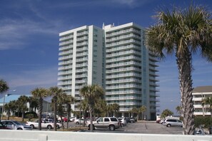 Een hoog hotel met diverse balkons, een parkeerplaats en palmbomen.