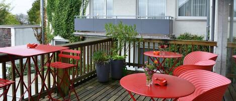 An outdoor patio with red metal furniture, potted plants, and a view of a building with windows.