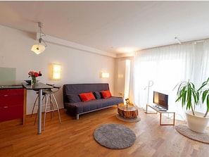 A modern living room with a sofa, a dining table, a TV, and a potted plant.