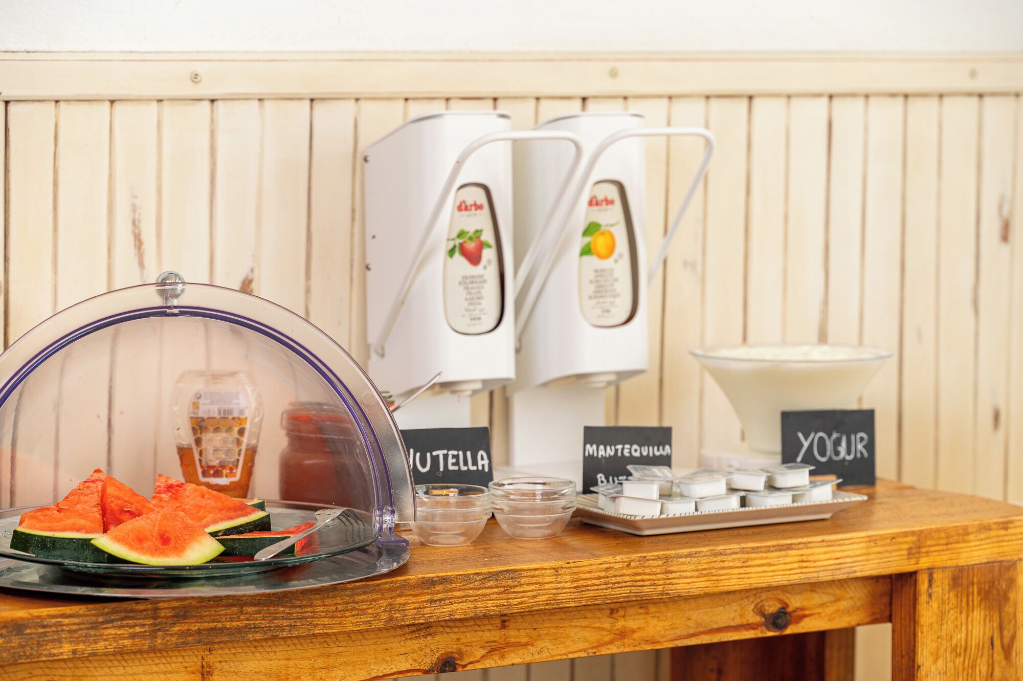 Una estación para el desayuno con una exhibición de sandía, un dispensador de yogur y una máquina de café.