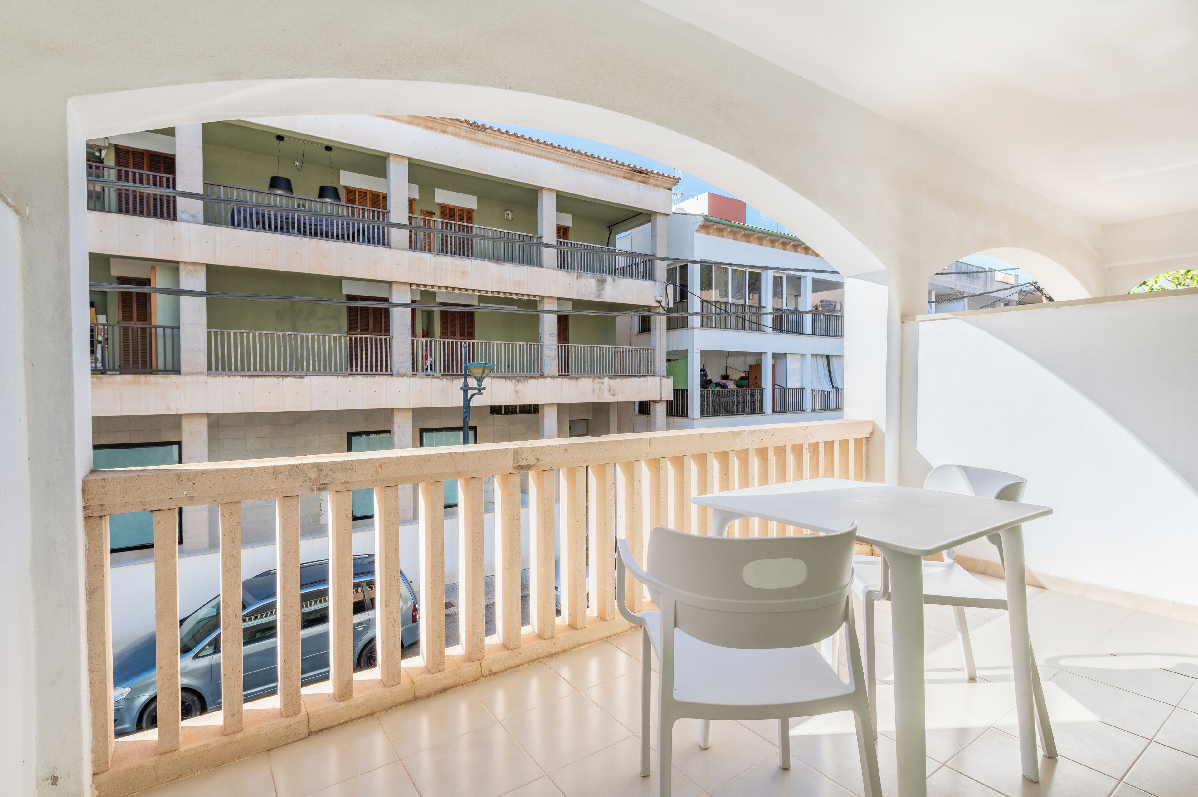 Un edificio residencial de varios niveles con balcones, un comedor con mesa y sillas, y vista a coches estacionados.