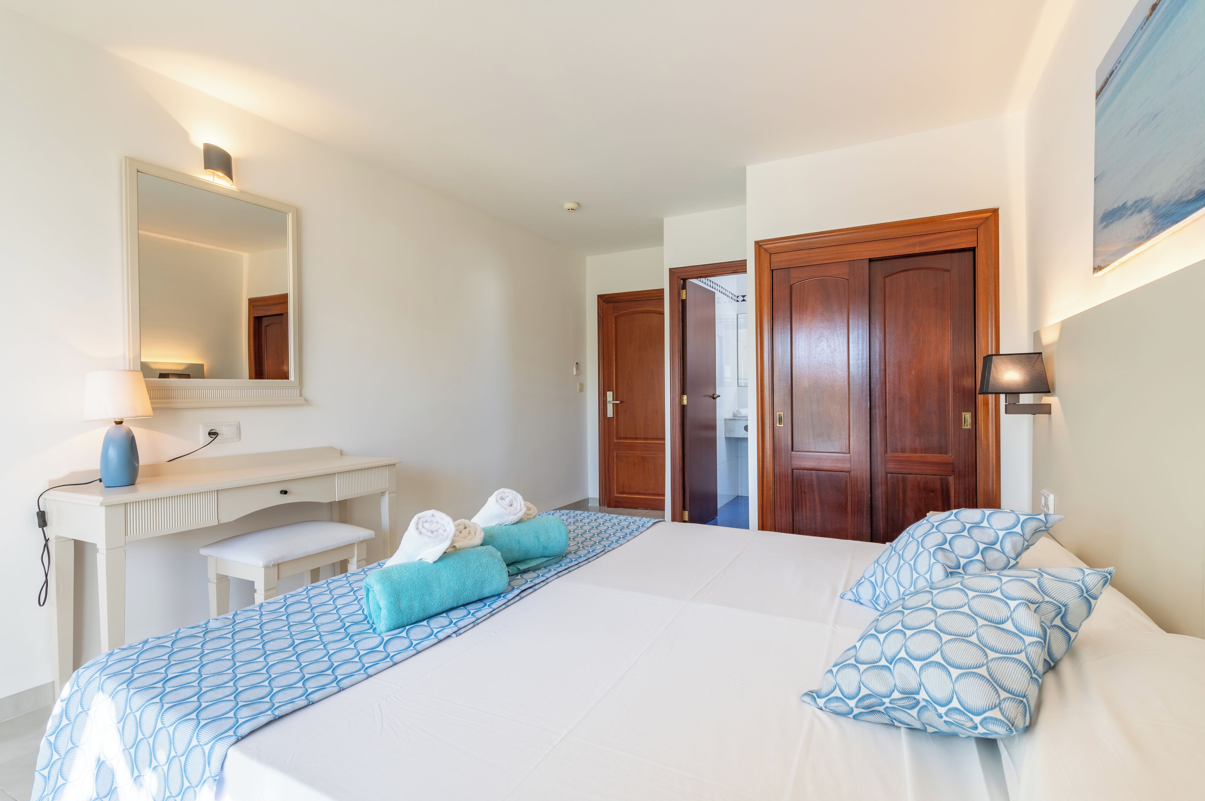 A hotel room with a bed, a desk, a mirror, and a door.