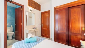 Quarto de hotel com uma cama, banheiro com vaso sanitário e pia, e portas de madeira.